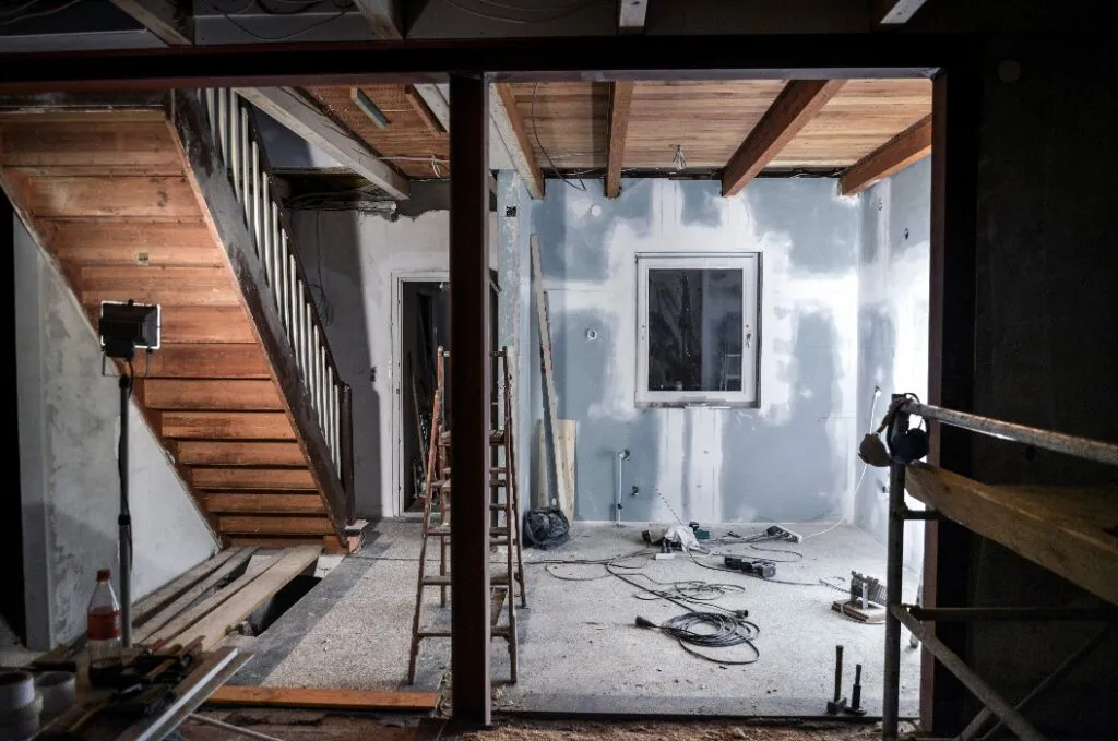 Eine unfertige Baustelle mit grauer Wand, Holztreppe und verstreuten Werkzeugen