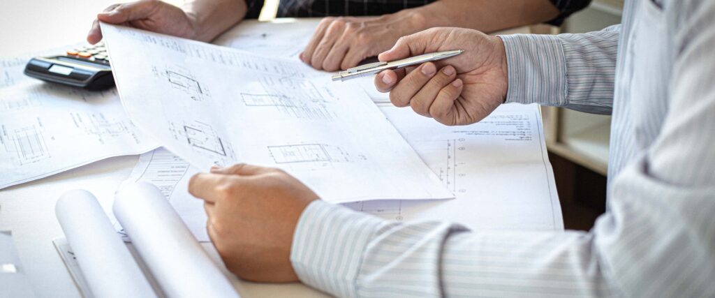 Zwei Personen begutachten konzentriert Baupläne auf einem weißen Schreibtisch