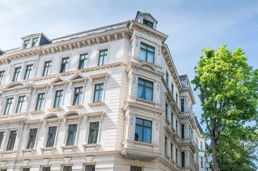 Helles historisches Gebäude mit reich verzierten Fassaden und grünen Bäumen davor